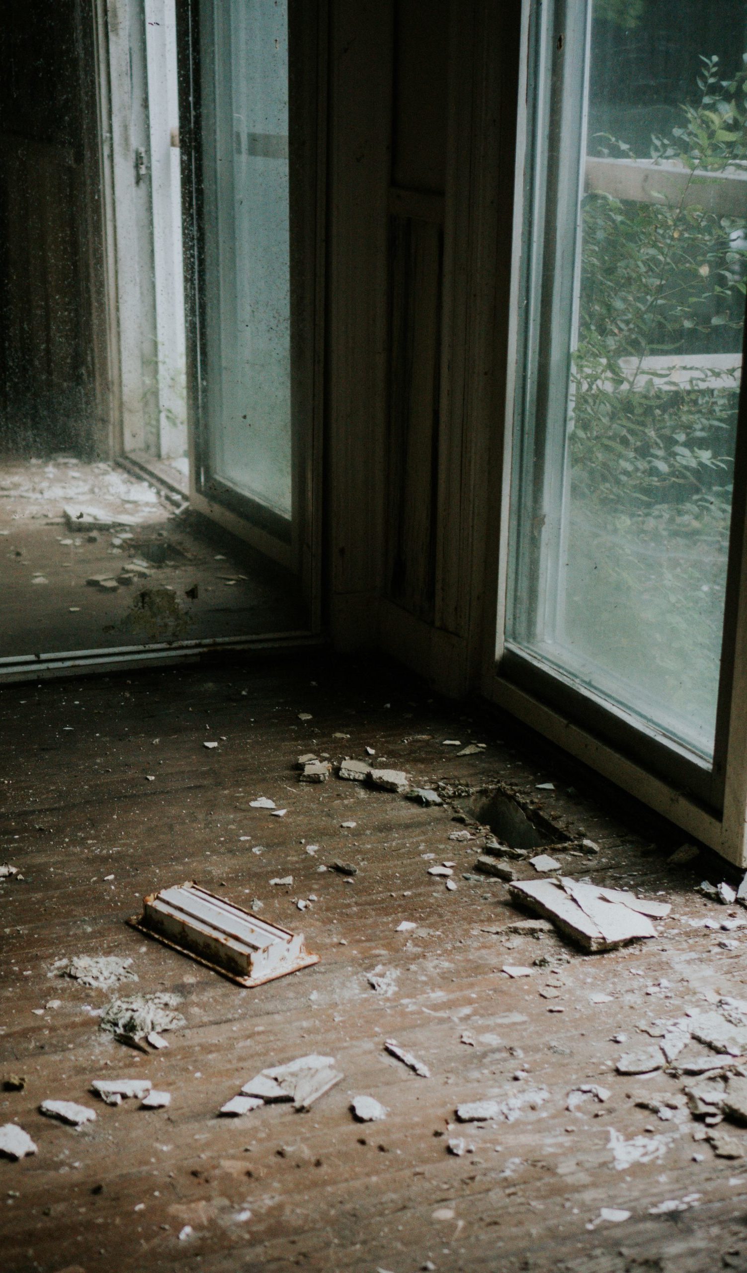 A broken window and debris on the floor of an abandoned house.