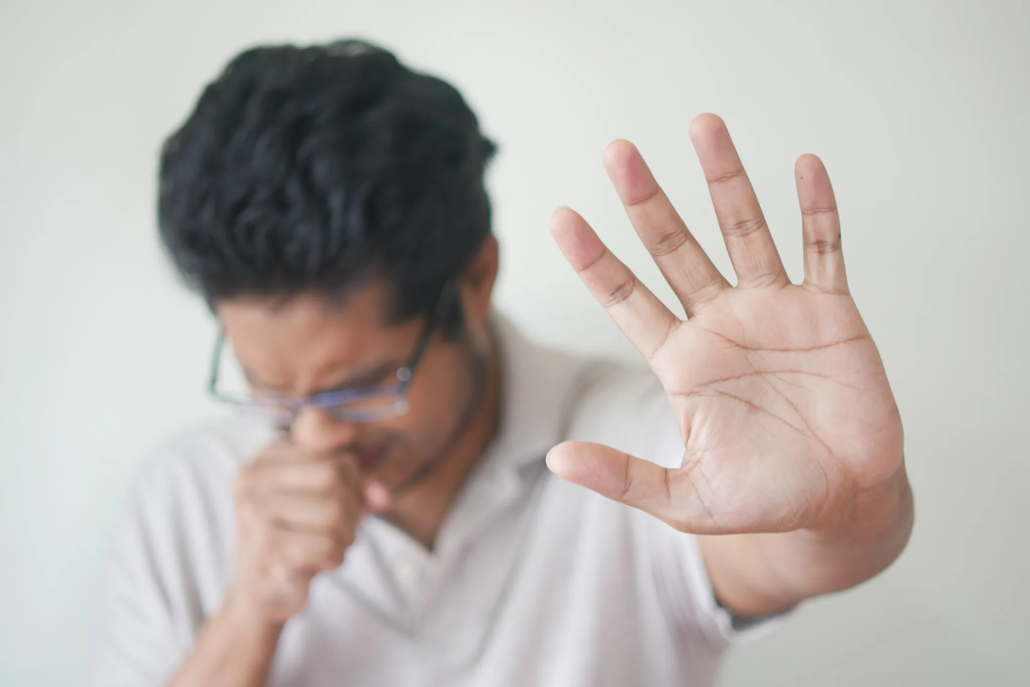 A man with glasses is holding his hand up to the side of his face.
